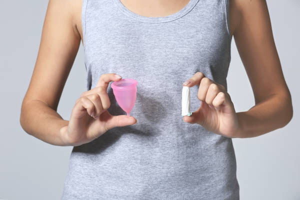 Frau hält Menstruationstasse und Tampon in den Händen