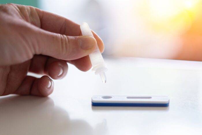 Jemand tropft Flüssigkeit auf einen Antigen-Schnelltest.