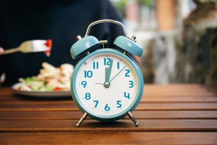Wecker auf dem Tisch, Teller mit Essen im Hintergrund.