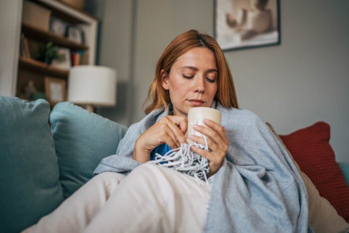 Frau mit Deck auf Couch und Tasse in ihren Händen